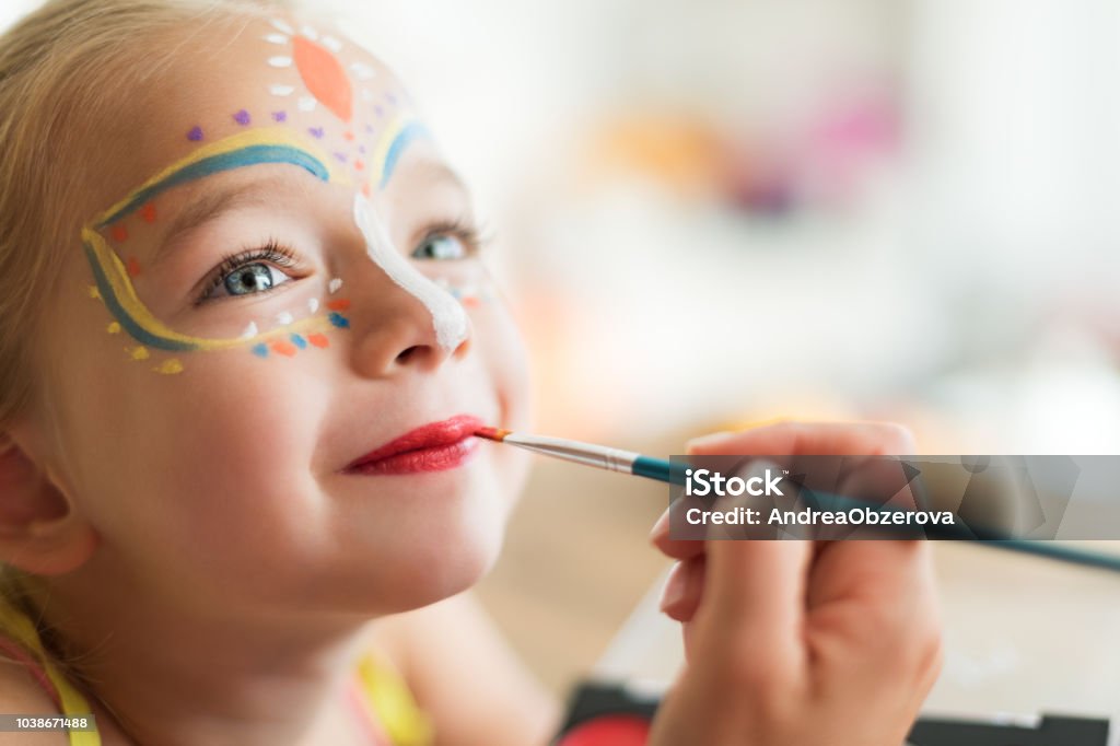 Menina bonitinha ter seu rosto pintado para a festa de Halloween. Halloween ou carnaval fundo de estilo de vida familiar. Enfrentar a pintura, headshot close-up. - Foto de stock de Criança royalty-free