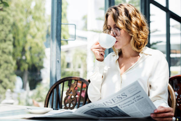 mujer de negocios, leer el periódico por la mañana - mujer leyendo periodico fotografías e imágenes de stock