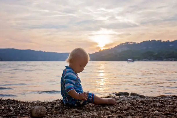 Photo of Cute child, toddler boy, enjoying the sunset over a lake