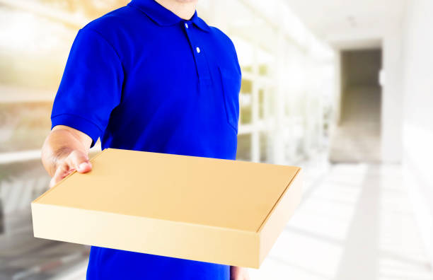 istock Delivery man in blue uniform and holding paper box with delivering package on office background. Concept fast delivery service or order online shopping and express delivery. 1038700490