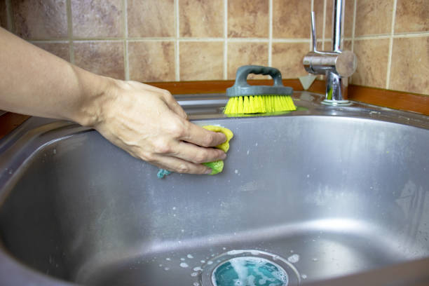 istock Woman's cropped hands washes and cleans a sink with a sponge and brush. 1038700706