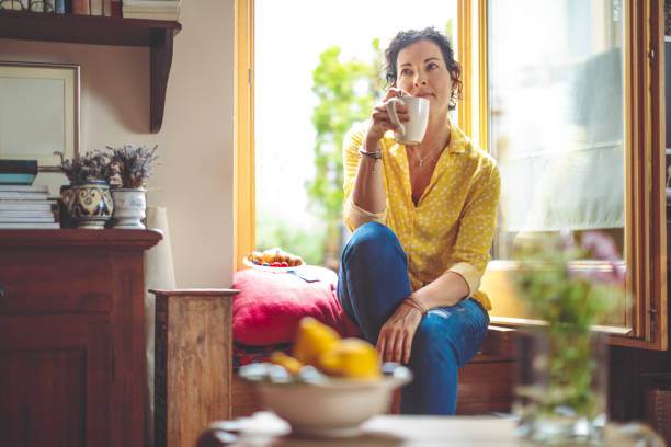 mujer madura es tener el café de la mañana en casa - tea women cup drinking fotografías e imágenes de stock