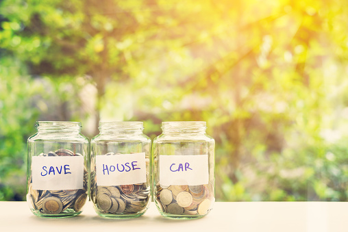 Saving money for house and car concept : Coins in three jars with label. Ideas of saving for a down payment on a car or home that allow buyers to use down payment to reduce overall cost of borrowing.