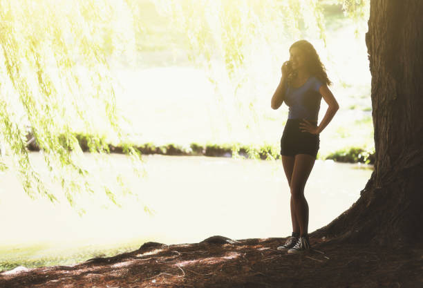 istock Young woman almost silhouetted under a sunlit willow tree 1038731176