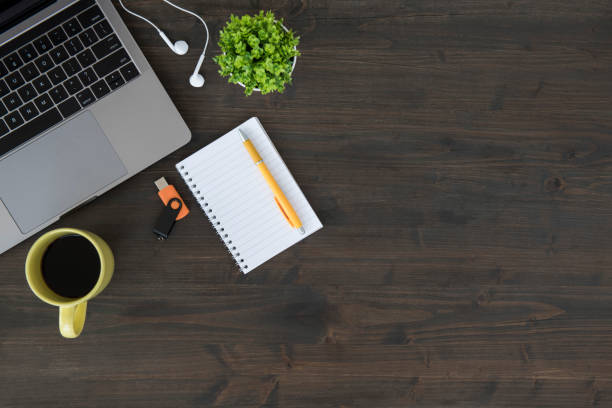 Overhead view of desk with various items Top view of wooden table with laptop, plant, headphones, coffee cup, note pad with pencil and USB device. usb stick photos stock pictures, royalty-free photos & images