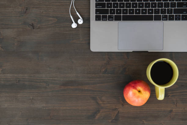 Top view of wooden table with laptop, peach, headphones and coffee cup.