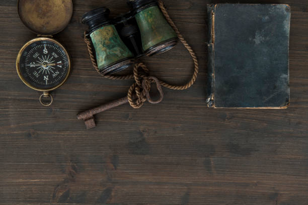 This image depicts a collection of vintage items, evoking a sense of nostalgia and historical charm. The focus is on an old-fashioned handheld roller, possibly a printing or inking tool, resting on top of what appears to be a stack of aged books or documents. Surrounding this are other antique objects, including a small, ornate box with a wooden base and a metallic device, possibly an old-fashioned clock or telegraph receiver, that hints at the bygone era of mechanical innovation.The setting seems to be a dimly lit room or a museum, with warm, earthy tones that add to the vintage atmosphere. The background is softly blurred, drawing attention to the objects in the foreground while suggesting an environment rich with history. Each item in this scene tells its own story, collectively offering a glimpse into the past and the tools and artifacts that were once part of daily life.