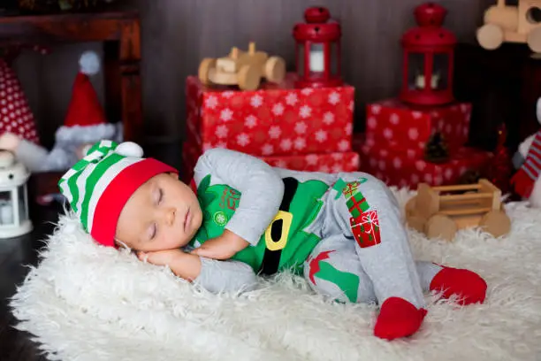 Photo of Sweet toddler child, boy, sleeping with lots of toys, dressed like an elf