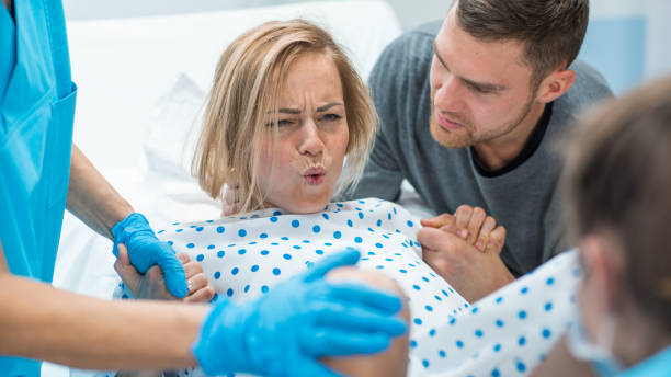 in the hospital woman in labor pushes to give birth, obstetricians assisting, husband holds her hand for support. modern delivery ward with professional midwives. - labour room imagens e fotografias de stock