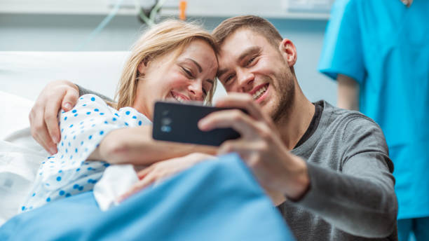 Father Takes Selfie of Him with His Wife Holding Newborn Baby while Lying on the Hospital Bed. Happy Young and Smiling Family. Father Takes Selfie of Him with His Wife Holding Newborn Baby while Lying on the Hospital Bed. Happy Young and Smiling Family. labor childbirth photos stock pictures, royalty-free photos & images
