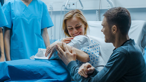 En el Hospital madre espera recién nacido bebé, apoyo padre abrazando con amor a bebé y esposa. Familia feliz en la sala de entrega moderna. photo