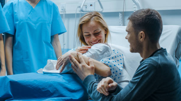 in the hospital mother hold newborn baby, supportive father lovingly hugging baby and wife. happy family in the modern delivery ward. - women group of people lying down mother imagens e fotografias de stock