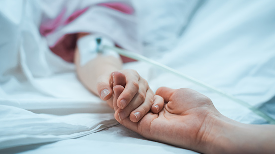 Recuperación niño pequeño acostado en la cama del Hospital para dormir, la madre sostiene su mano reconfortante. Se centran en las manos. Emotivo momento familiar. photo