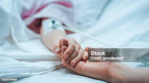 Recovering Little Child Lying In The Hospital Bed Sleeping Mother Holds Her Hand Comforting Focus On The Hands Emotional Family Moment Stock Photo - Download Image Now