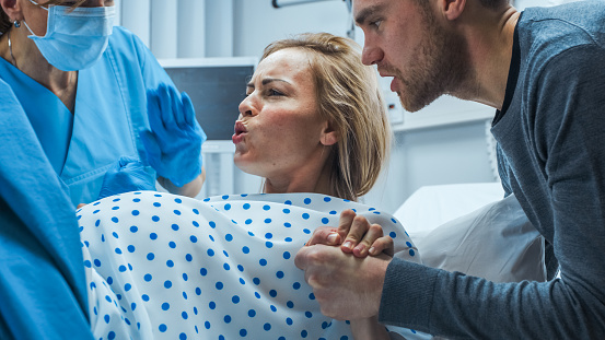 En el Hospital, cerca a una mujer en trabajo empujando con fuerza dar a luz, ayudar a obstetras, cónyuge sostiene su mano. Moderna maternidad Hospital con parteras profesionales. photo