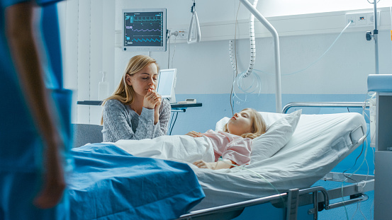 Sick Little Girl Lying in the Hospital Bed Sleeping, Her Mother Worries and Prays Beside Her. Emotional and Spiritual Moment Full of Hope.