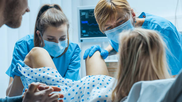 nell'ospedale donna in travaglio spinge per partorire, ostetrici che assistono, il marito tiene la mano. reparto consegne moderno con ostetriche professionali. retro visualizza metraggio. - human pregnancy obgyn women child foto e immagini stock