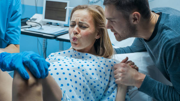 in the hospital close-up on woman in labor pushes to give birth, obstetricians assisting, husband holds her hand. modern delivery ward with professional midwives. - women group of people lying down mother imagens e fotografias de stock