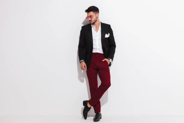 relaxed elegant man leaning against wall looks down to side relaxed elegant man wearing a black suit is leaning against a white wall and looks down to side while standing with legs crossed, full body picture legs against the wall stock pictures, royalty-free photos & images