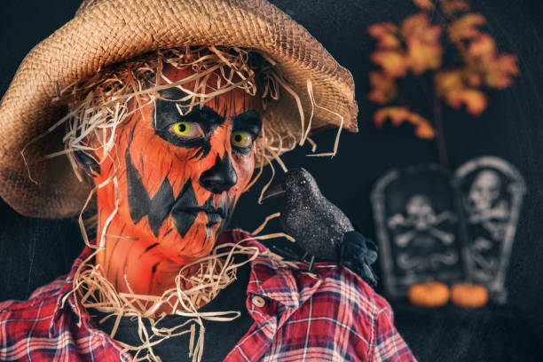 A person painted as a scary pumpkin scarecrow with a crow on the shoulder.