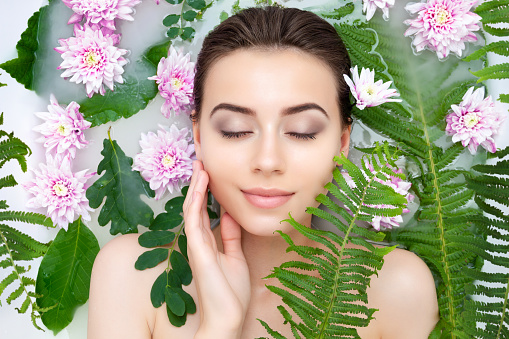Portrait of young sexy beauty female woman smiling with clean pure skin taking spa relaxing in bath with flowers and green leafs white soap water. Skin beauty health care concept. Body part and nature
