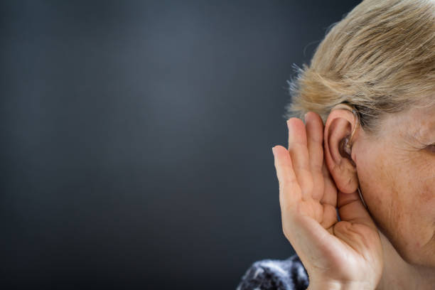 istock Elderly woman with hearing aid on black, grey background. Deafness concept. 1038832462