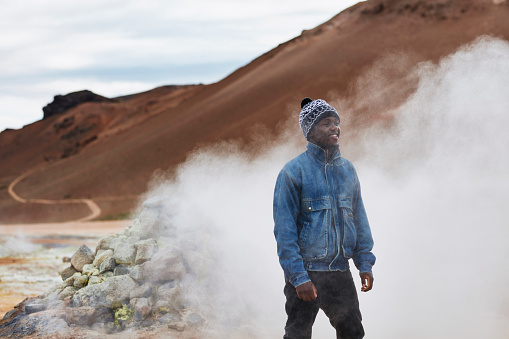 Young man posing on a geothermal area. Geysers and steam vents in background