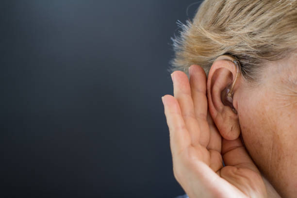 istock Elderly woman with hearing aid on grey background. Deafness concept. 1038835640