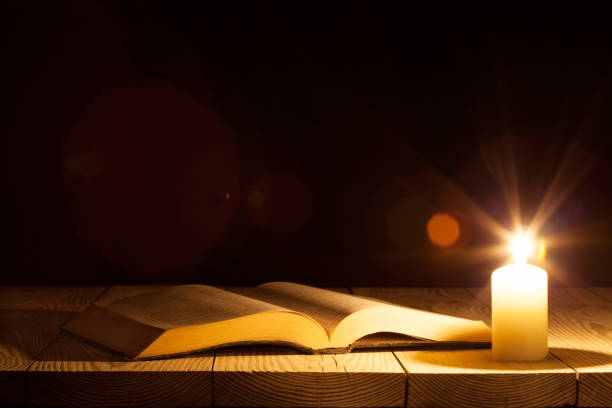 a bible on the table in the light of a candle stock photo