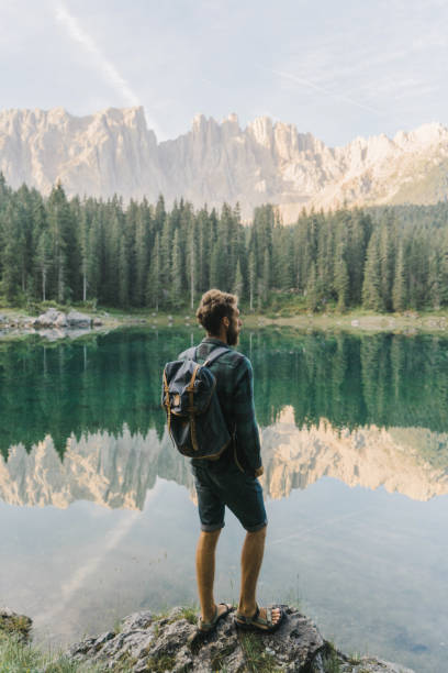 uomo in piedi e guardando il lago di carezza nelle dolomiti - latemar mountain range foto e immagini stock