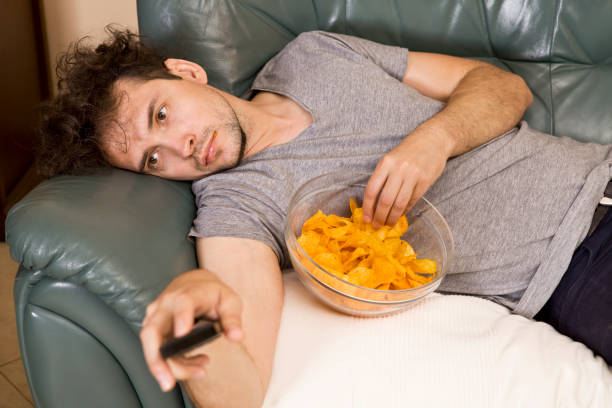 Lazy man with the remote and chips on the couch Man's relax after work, beer and chips. Lazy man laziness stock pictures, royalty-free photos & images