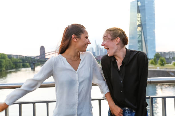 istock Girlfriends Standing on City Bridge Over River Looking at Each Other and Laughing 3 1038881130