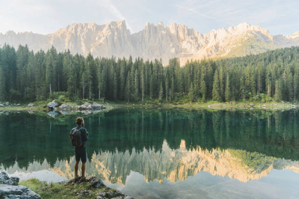 uomo in piedi e guardando il lago di carezza nelle dolomiti - latemar mountain range foto e immagini stock