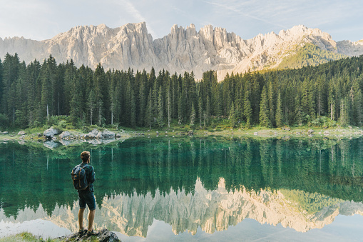 Young Caucasian man standing and looking at  Lago di Carezza in Dolomites