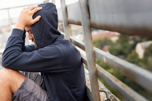 Depressed man holding head in hands Depressed, desperate young man sitting on the building rooftop terrace, wearing hoodie, holding head in hands post traumatic stress disorder photos stock pictures, royalty-free photos & images