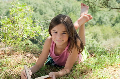 Cute Little Blond Girl Reading Book Outside on Green Grass Lawn.