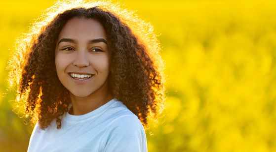 Beautiful mixed race African American girl teenager female young woman smiling and happy in a field of yellow flowers
