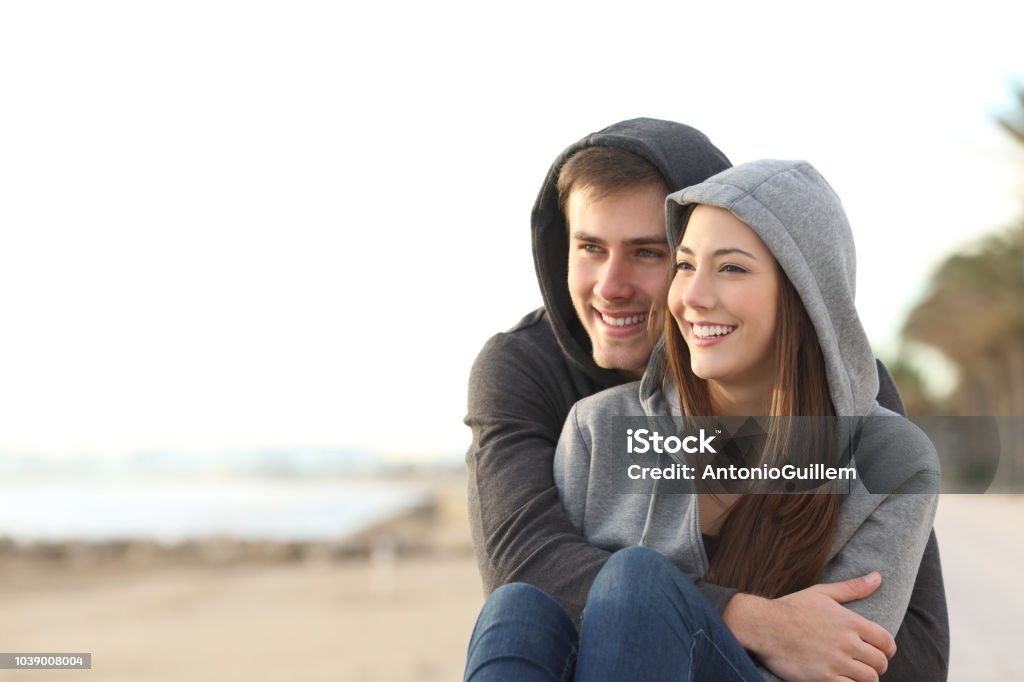 Couple of teens looking at horizon on the beach Happy couple of teens hugging and looking at horizon on the beach Teenager Stock Photo