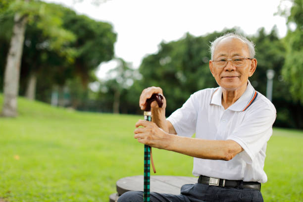 Senior man wearing suit and flat cap enjoying music with earphones while sitting on a park bench