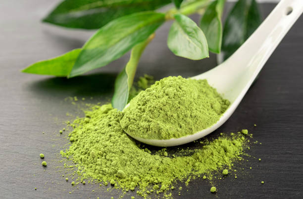 Matcha powder in White ceramic spoon and tea leaves on black background