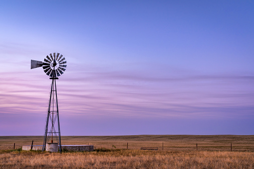 windmill with a pump and cattle water tank in shortgrass prairie, Pawnee National Grassland in northern Colorado, summer dusk scenery