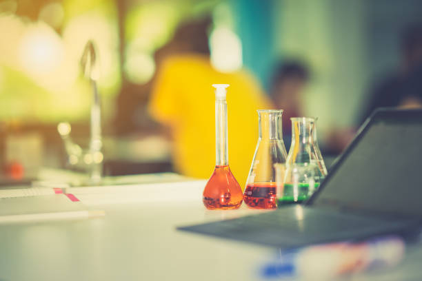Glassware chemistry science laboratory on table and blurred tablet on blurred student in classroom
