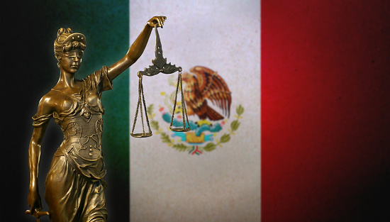 Close-up of a small bronze statuette of Lady Justice before a Mexican flag.