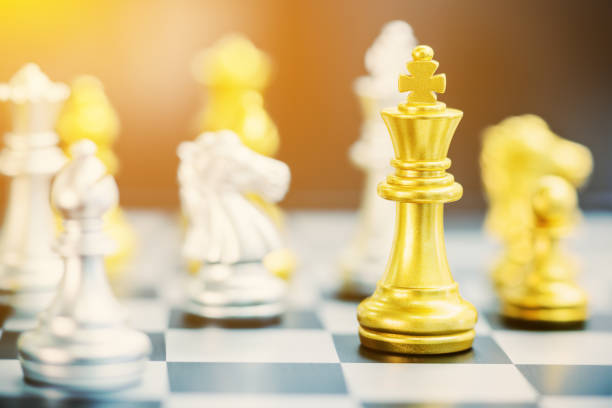 Leader or winner / conqueror concept : Side view of gold / golden king chess piece with silver knight and bishop nearby, on a black white 8x8 grid chessboard. Chess is a two player strategy board game líder o ganador / el concepto de conquistador: vista lateral del rey oro / oro pieza de ajedrez con el caballero de plata y el obispo, en un tablero de rejilla negro blanco 8 x 8. el ajedrez es un juego de mesa de estrategia de dos jugadores