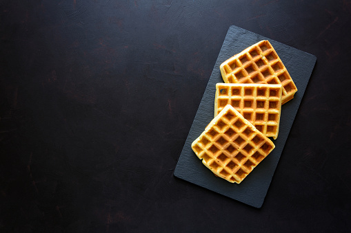 Belgian waffles on slate plate on dark wooden background. Top view. Copy space
