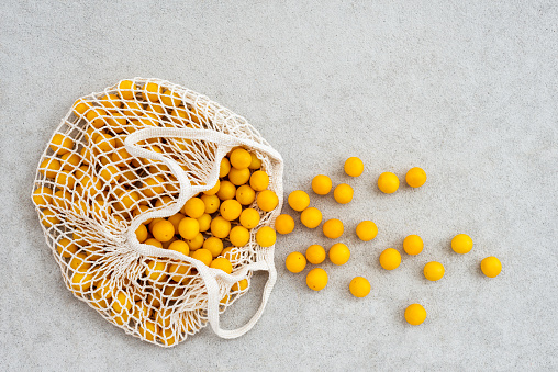 Lots of yellow plums in a cotton mesh shopping bag, on concrete background.