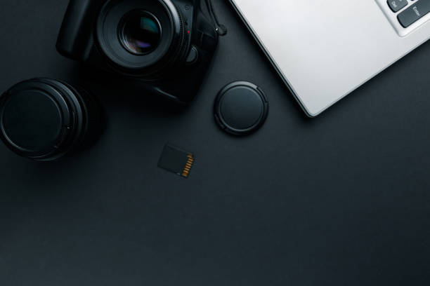 istock Work space on black table of photographer. Minimal workspace with Laptop, camera and lens copy space on dark background. Modern and elegant. Top view. Flat lay style. 1039158932