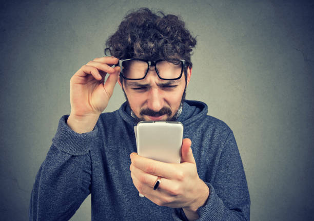uomo che indossa occhiali con problemi a vedere il messaggio del cellulare - strizzare gli occhi foto e immagini stock