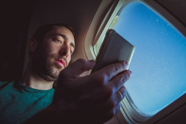 istock Young man looking at his smartphone and using it while seating by the window of an airplane 1039209910