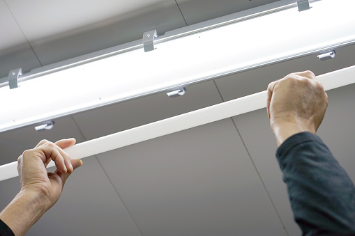 Electric hands changing ceiling fluorescent lamp. The concept of repair and service.